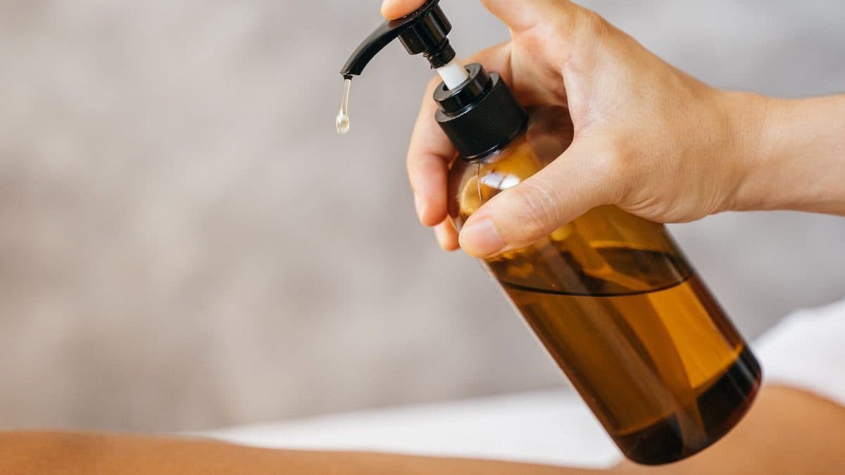 Main pressant un flacon d’huile de massage au-dessus d’une table de soin